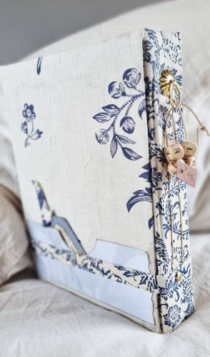 Dos d'un carnet artisanal créé par Isabelle Morot-Sir, confectionné à la main avec des matériaux recyclés et une couverture en tissu bleu et blanc.