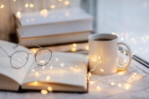 Livres ouverts, tasse de café et lunettes dans une ambiance chaleureuse évoquant le plaisir de la lecture.