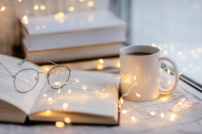 Livres ouverts, tasse de café et lunettes dans une ambiance chaleureuse évoquant le plaisir de la lecture.